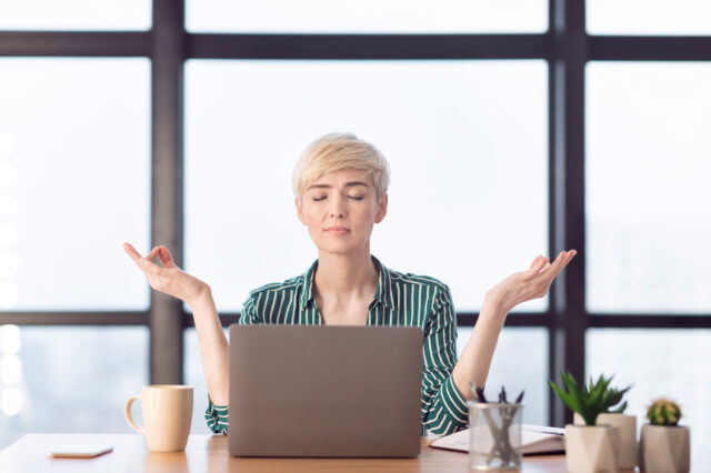 Meditation auf der Arbeit, eine Geschäftsfrau entspannt vor dem Laptop.