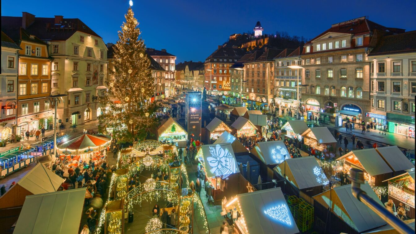 (c) Region Graz | Robert Maybach Der Adventmarkt am Grazer Hauptplatz aus der Vogelperspektive. Es ist dunkel und man sieht viele glitzernde Beleuchtungen.