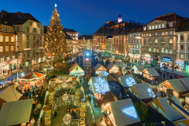 (c) Region Graz | Robert Maybach Der Adventmarkt am Grazer Hauptplatz aus der Vogelperspektive. Es ist dunkel und man sieht viele glitzernde Beleuchtungen.