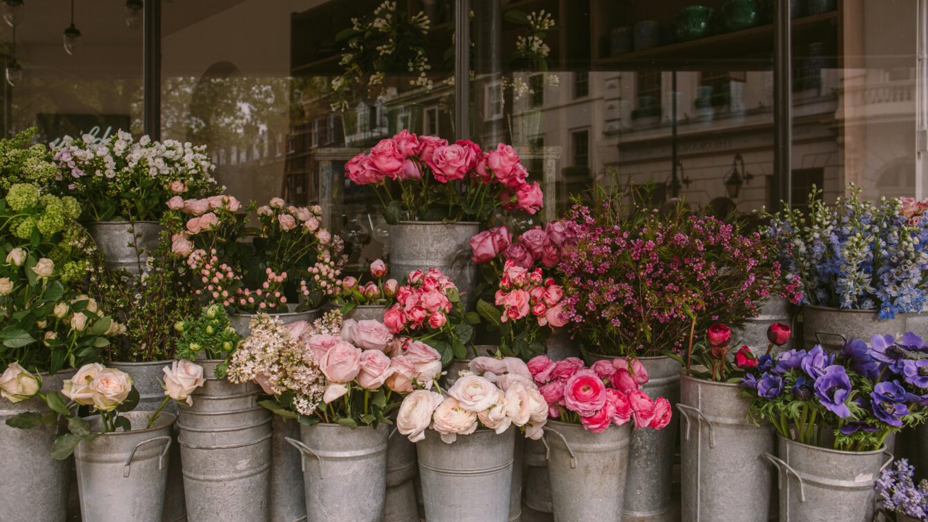 (c) Alisa Anton | Unsplash Foto von vielen Eimern mit bunten Blumen gefüllt vor einer Festerfront.
