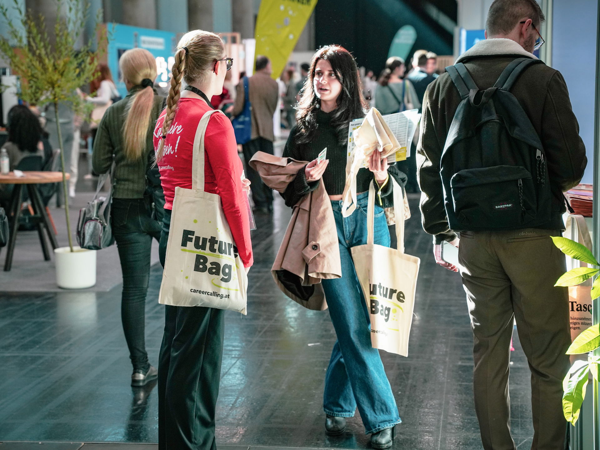 Zwei junge Frauen unterhalten sich auf der Career Calling Messe. Sie halten gratis Goodiebags in der Hand.