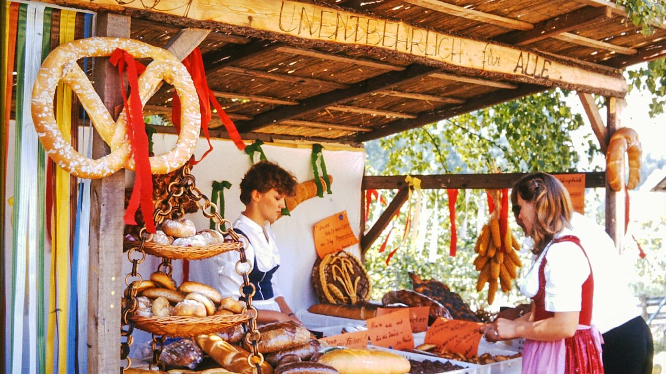 (c) Bernhard | Unsplash Menschen in Tracht an einem Marktstand, der Gebäck verkauft.