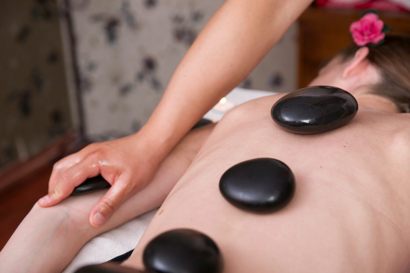 Person erhält eine Hot-Stone-Massage; mehrere glatte schwarze Steine liegen auf dem Rücken, während ein Arm massiert wird