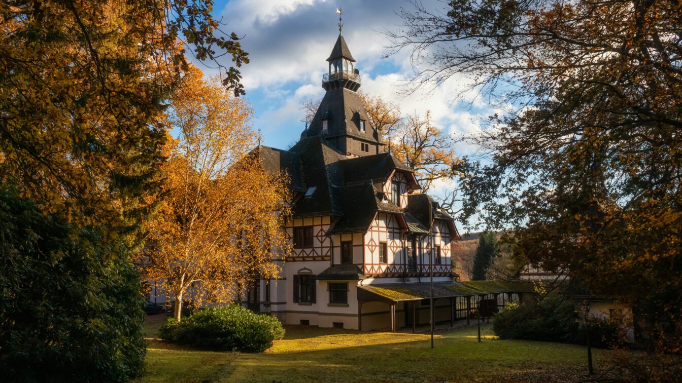 (c) Evgeni Tcherkasski | unsplash Malereisches Fachwerkhaus inmitten herbstlich gefärbter Bäume im Sonnenschein, idealer Ausflugsort in Deutschland im Herbs