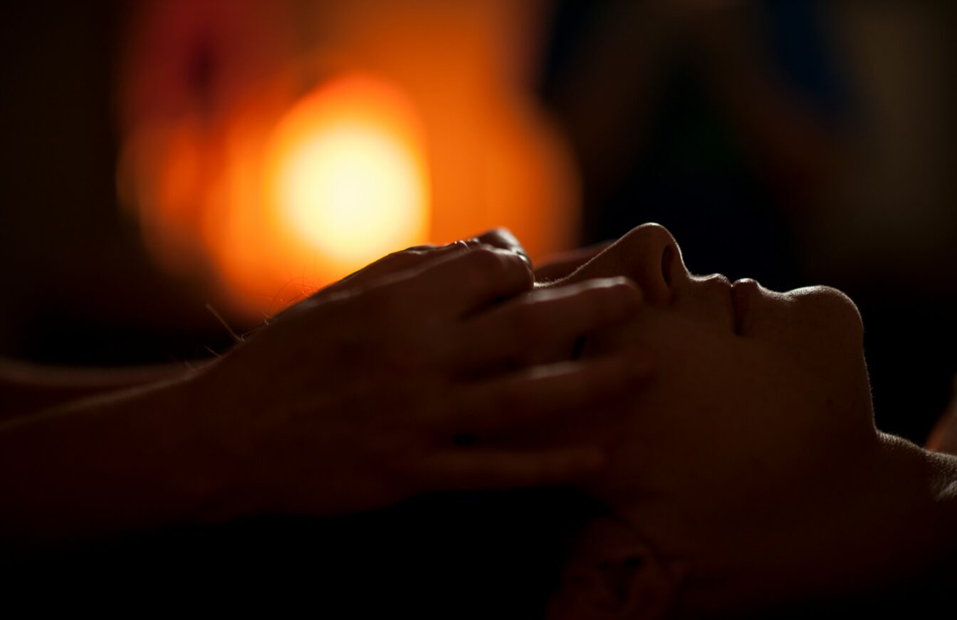 Person erhält eine entspannende Gesichtsmassage in einem stimmungsvoll beleuchteten Raum mit warmem Kerzenlicht im Hintergrund.