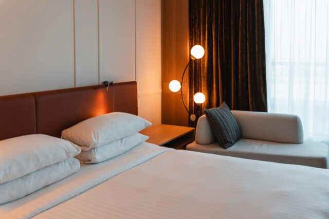 Ein gemachtes Hotelbett mit gemütlichem Licht und Vorhängen zum Balkon.