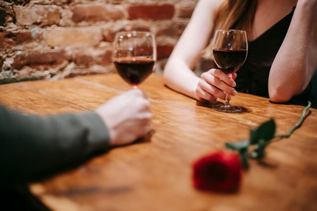 Romantische Lokale für Dates im Herbst und Winter in Wien: Zwei Personen mit Rotwein in Gläsern und einer Rose am Tisch