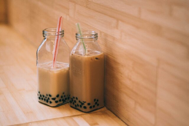 (c) Rosalind Chang | unsplash Zwei Glasgefäße mit Bubble Tea bestehend aus braunem Tee und schwarzen Boba-Perlen stehen auf Holzvertäfelung.