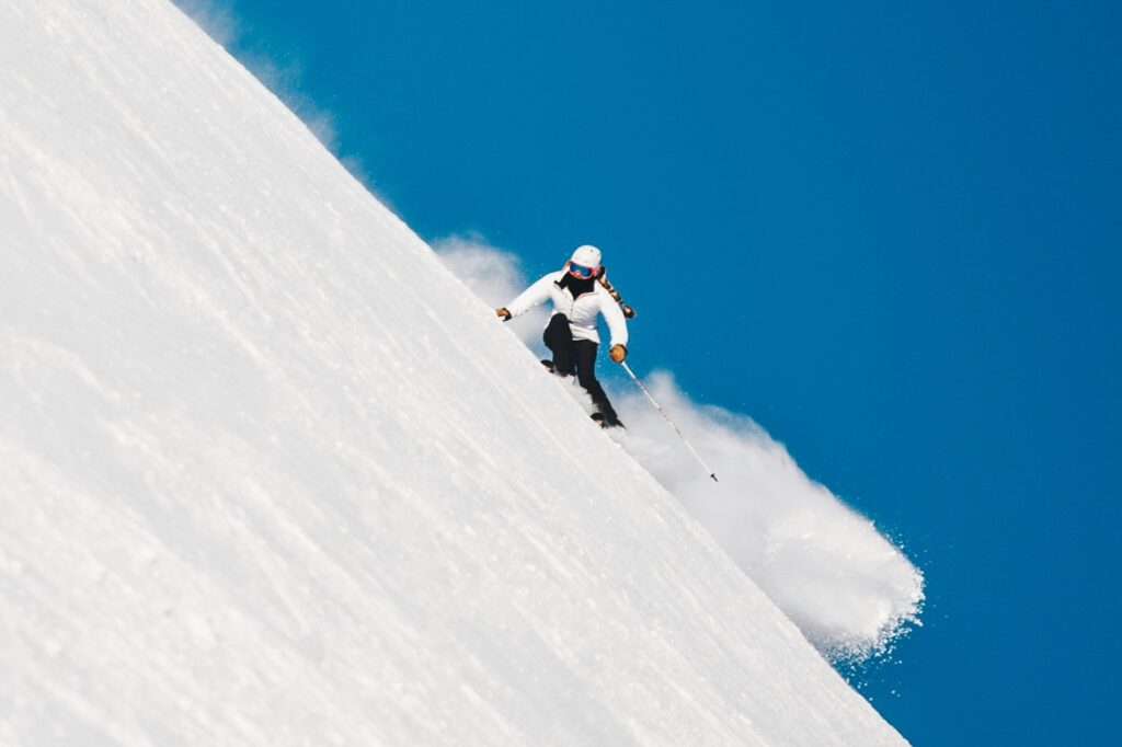 Skifahren in Bayern auf einer steilen Piste bei strahlend blauem Himmel – perfekte Wintersportbedingungen in beliebten Skigebieten wie Garmisch-Partenkirchen, Spitzingsee oder Sudelfeld, die bequem mit den Öffentlichen Verkehrsmitteln erreichbar sind.
