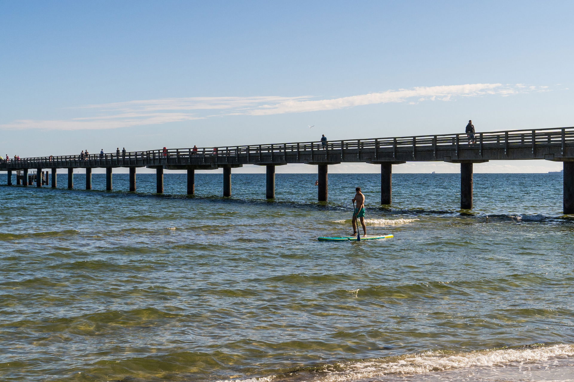 Ein Mann paddelt am Meer unter einer Brücke durch