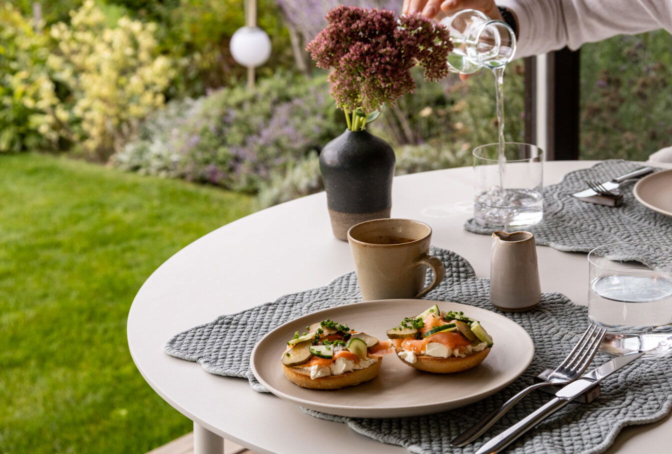 Frühstückstisch im Old School Guesthouse mit Bagels, Kaffee und Wasser, stilvoll gedeckt mit Blick ins Grüne.