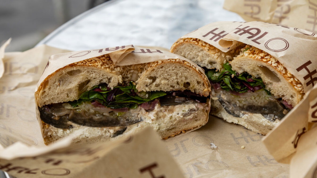 Vegetarisches Sandwich mit Sesambrötchen, gegrilltem Gemüse, Frischkäse und Salat, serviert in Papier gewickelt