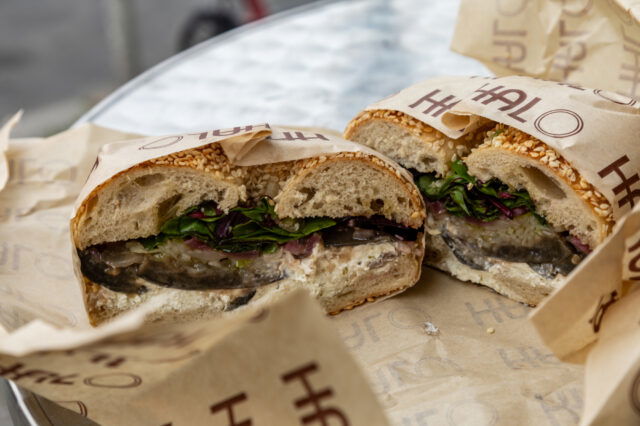 Vegetarisches Sandwich mit Sesambrötchen, gegrilltem Gemüse, Frischkäse und Salat, serviert in Papier gewickelt