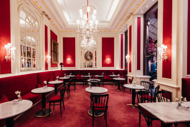 Blick auf die Einrichtung mit roten Samtbänken, Tischen und Luster im Café Sacher in Wien
