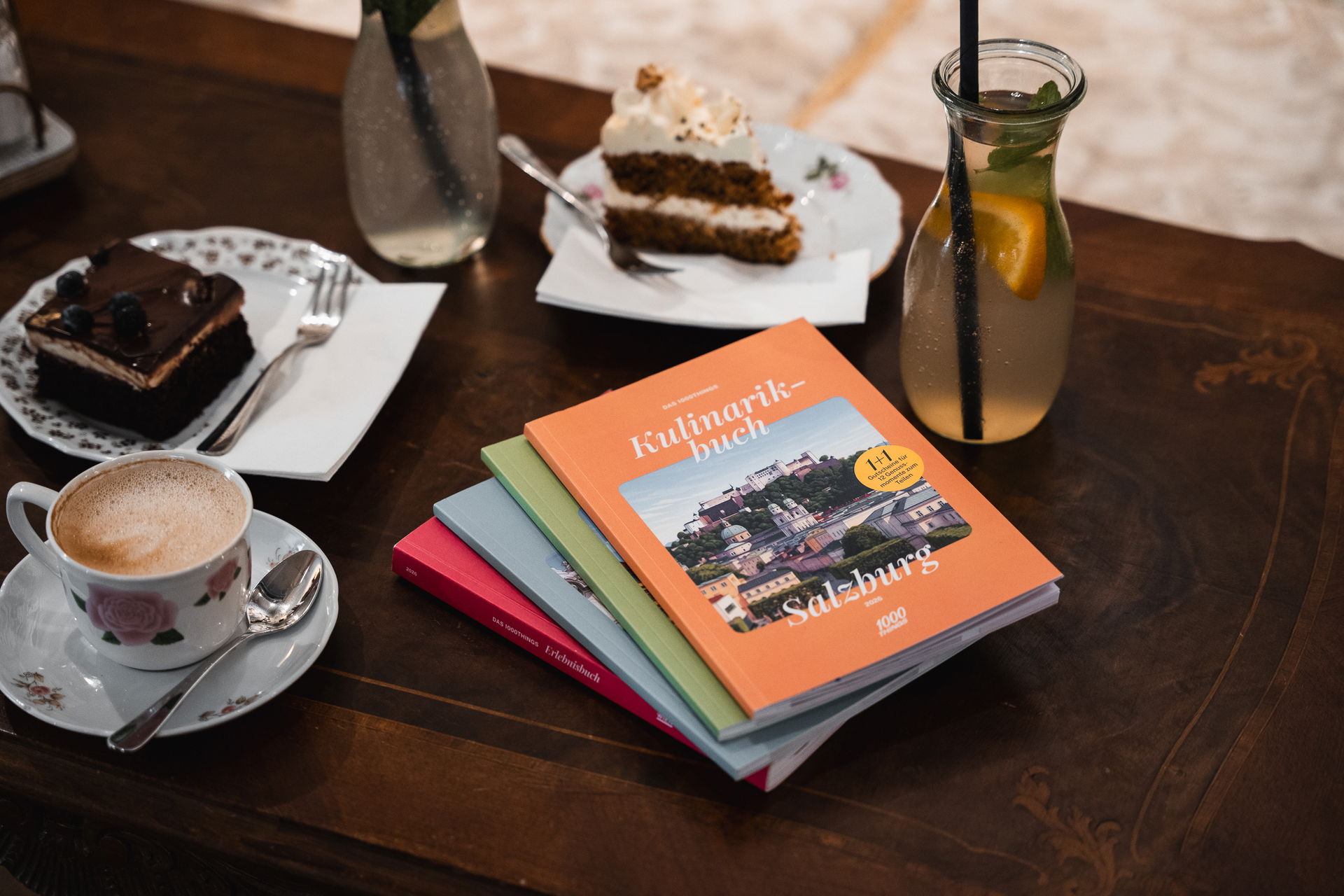 1000things Erlebnis- und Kulinarikbücher auf einem Tisch neben Kaffee und Kuchen