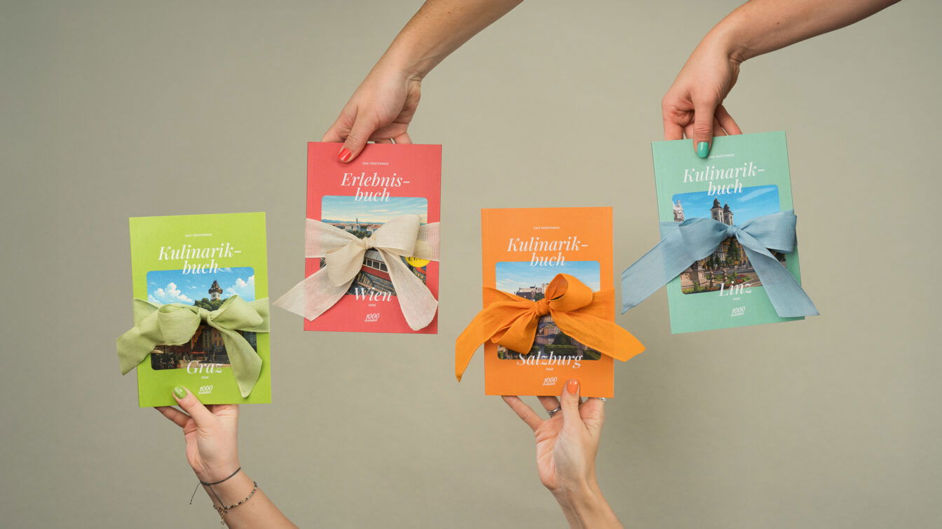 Vier Hände halten die 1000things Bücher – Erlebnisbuch Wien und Kulinarikbücher Graz, Salzburg und Linz – jeweils mit farbigen Geschenk-Schleifen.