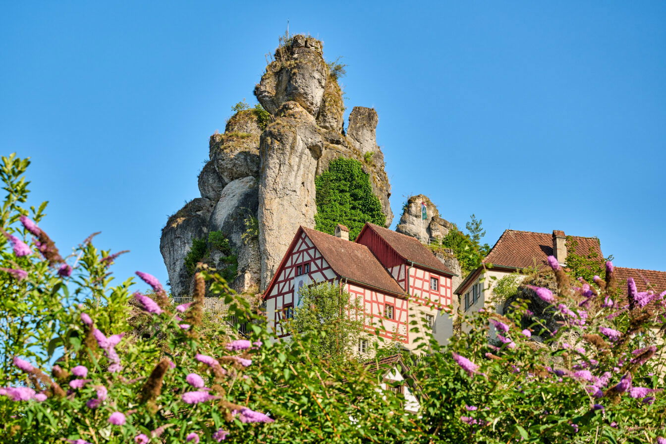 Fachwerkhäuser unter markanten Felsformationen in der Fränkischen Schweiz, Bayern, an einem sonnigen Sommertag.
