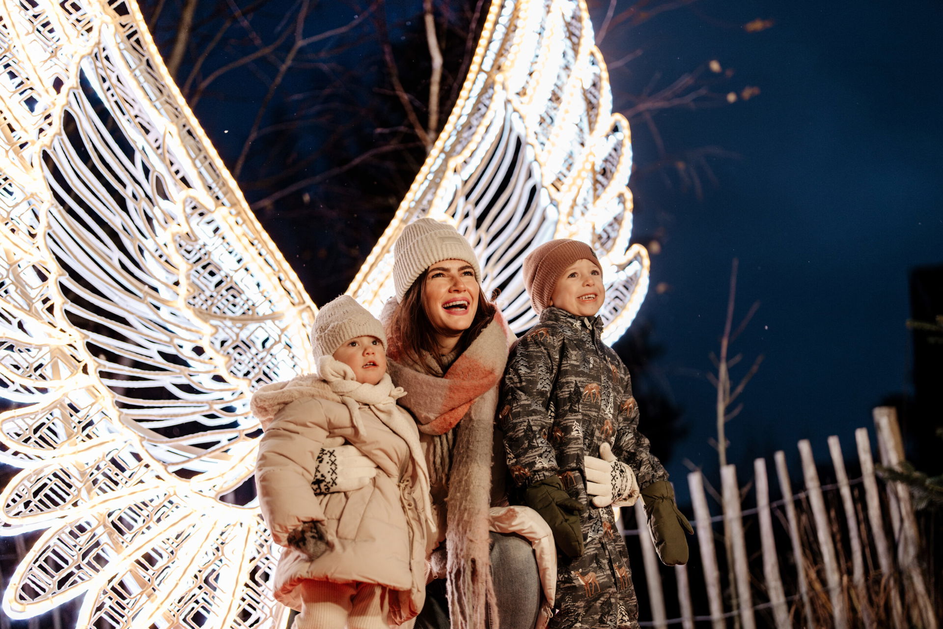 Mutter lächtelt mit Kindern in der zauberhaften Lichterwelt vor strahlender Engelsfigur (c) Studiosoco GmbH