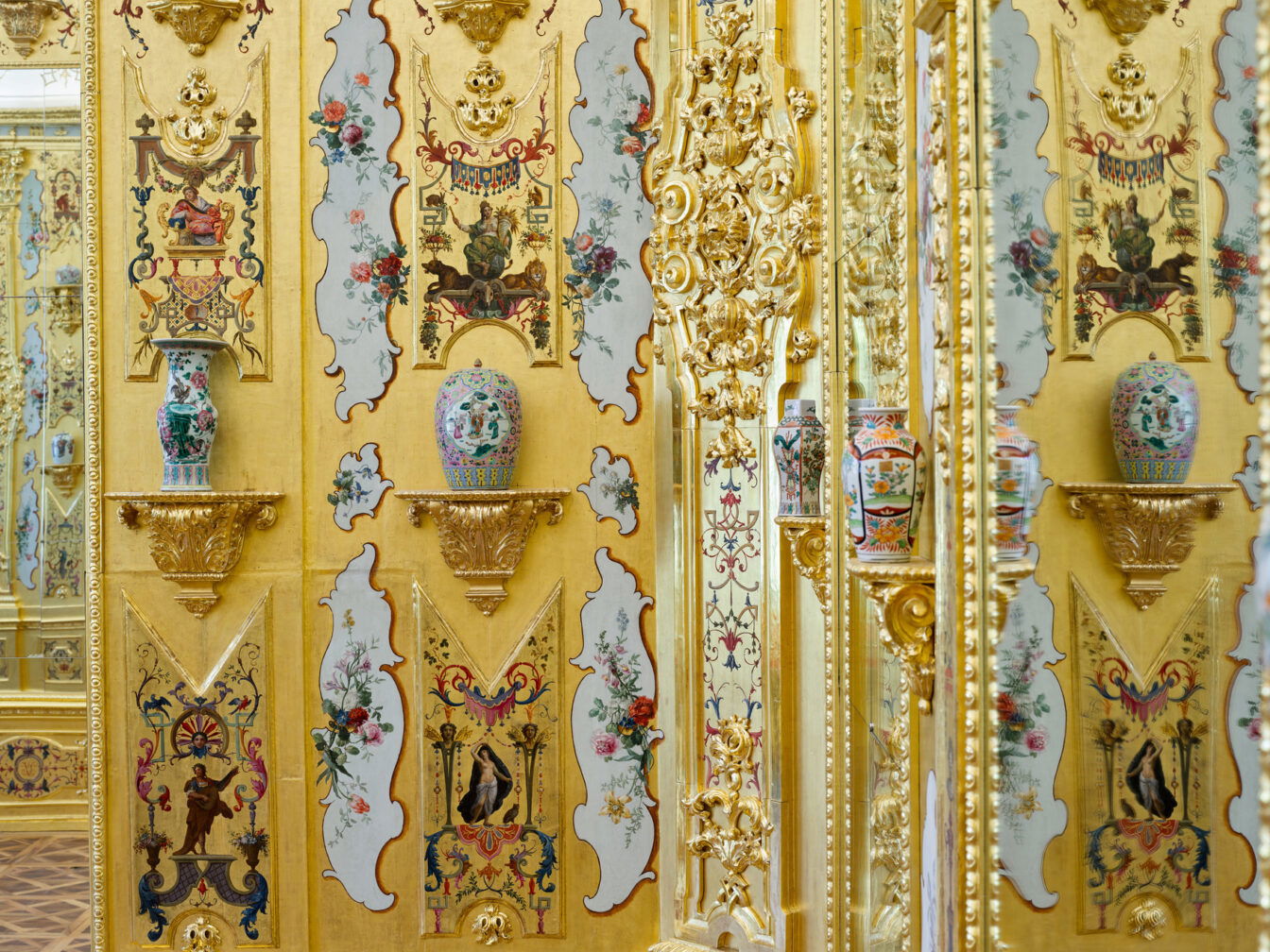 Innenansicht des Goldkabinetts im Unteren Belvedere in Wien. Die Wände sind vollständig vergoldet, mit floralen und figürlichen Malereien geschmückt und durch aufwendige Stuck- und Schnitzarbeiten verziert. Auf goldenen Wandkonsolen stehen bunte chinesische Porzellanvasen, die sich in den Spiegeln des Raums vervielfältigen.