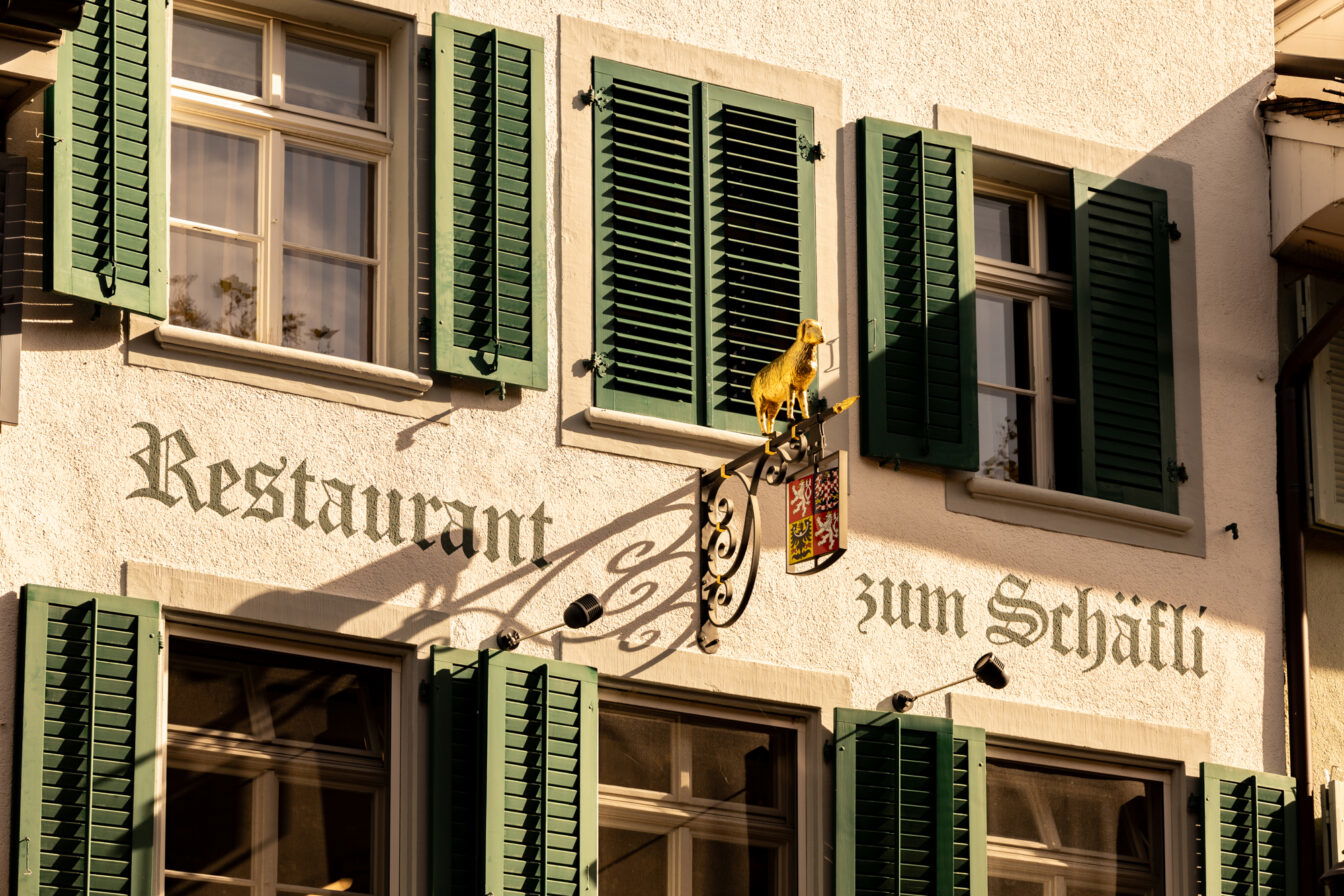 Fassade des Restaurants zum Schäfli in Winterthur mit grünen Fensterläden und dem goldenen Schaf als Wirtshausschild – ein traditionsreiches Highlight der Altstadt