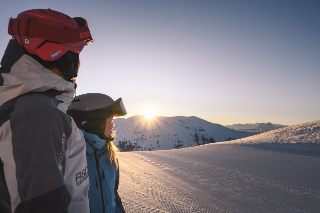 Zwei Personen auf Skipiste schauen in den Sonnenuntergang (c) Hochkönig Tourismus GmbH
