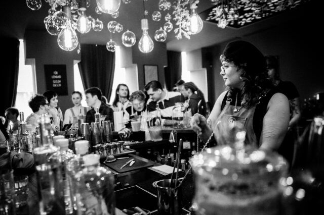 eine Frau steht hinterm Bartresen und mixt Cocktails