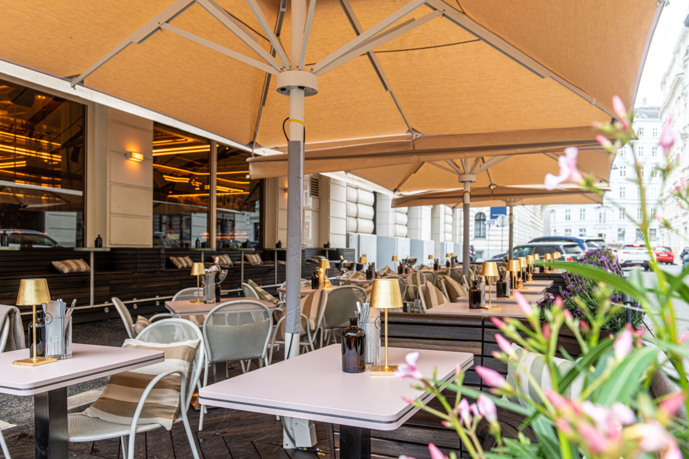 gedeckte Tische stehen unterm Sonnenschirm im Gastgarten der Bar Kleinod am Ring im 1. Bezirk in Wien