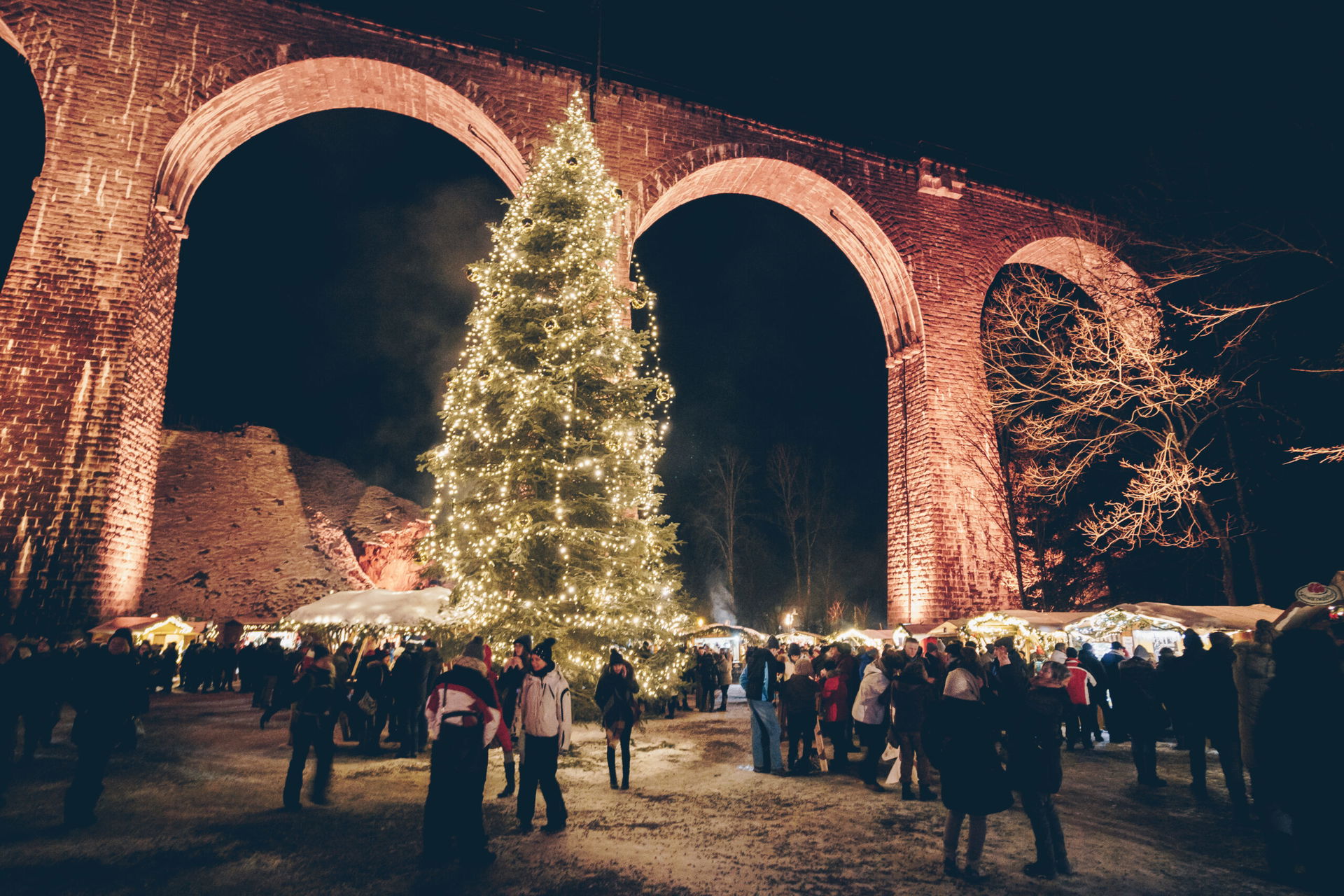 Weihnachtsmarkt in der Ravennaschlucht in Breitnau bei Stuttgart in Baden-Württemberg. Man sieht rießige Viadukt-Bögen mit einem Weihnachtsbaum davor.