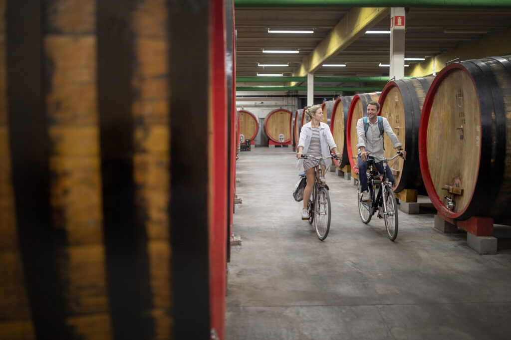 Zwei Personen fahren mit dem Fahrrad durch eine Brauerei