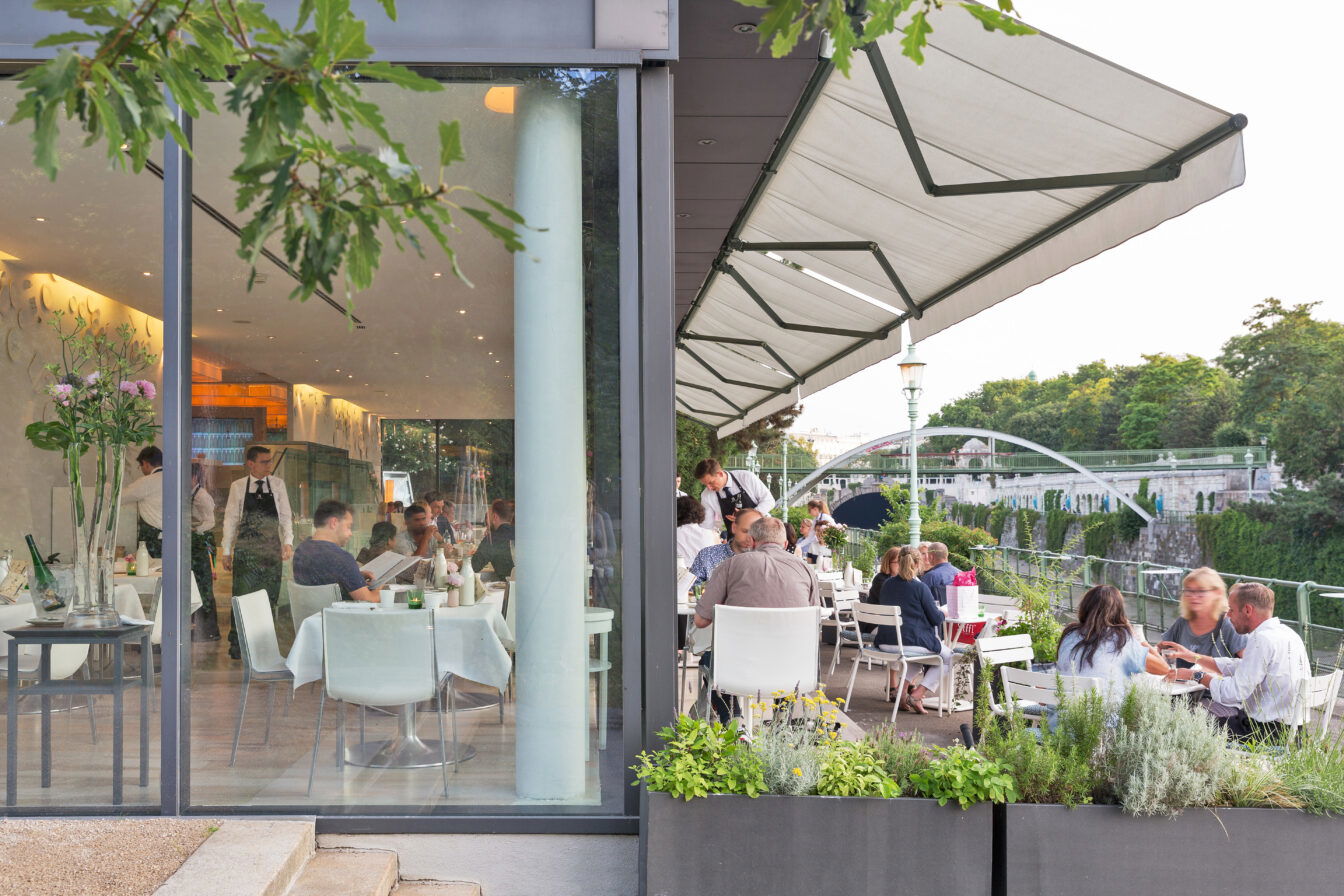 Blick auf besetzte Tisch im Inneren des Restaurants Meierei im Stadtpark in Wien sowie in den Gastgarten vor dem Lokal