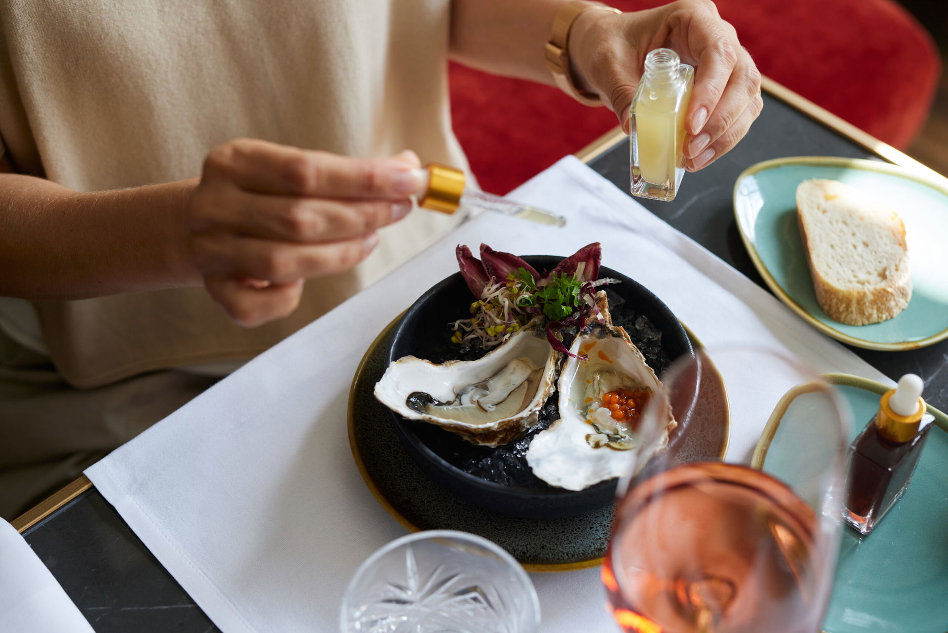 Teller mit Oyster und jemand, der mit einer Pipette etwas drauf dräufelt. Außerdem ist ein Glas Wein zu sehen. Es ist das Strandhotel Zingst an der Ostsee, in der Oyster Bar. 