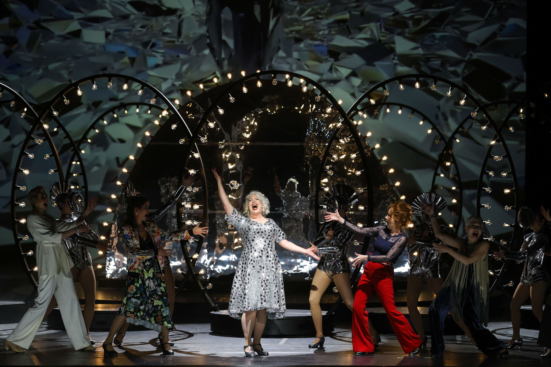 Performende stehen auf der Bühne in der Volksoper im Scheinwerferlicht und singen