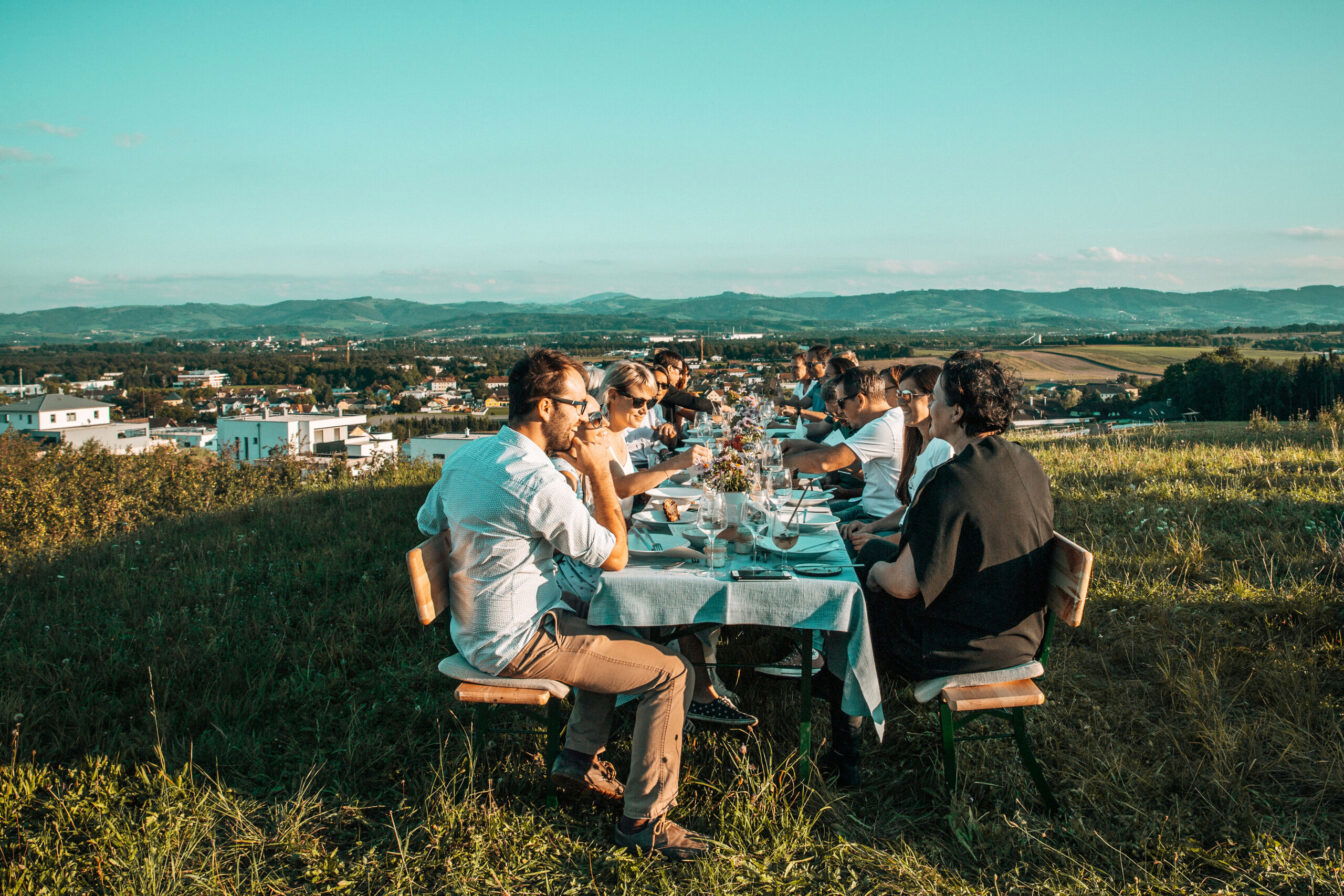 mehrere Menschen sitzen auf einem gedeckten Tisch in der Sonne bei einem Event der Mostviertler Feldversuche