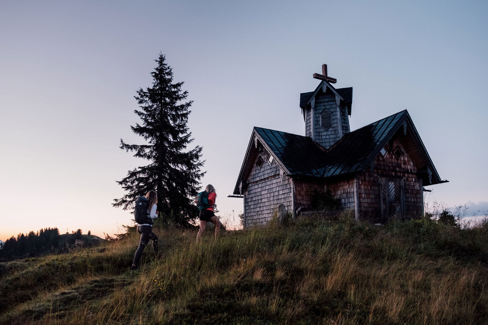 Zwei Wanderinnen gehen auf einem Berg in St. Johann in Salzburg auf eine Hütte zu.
