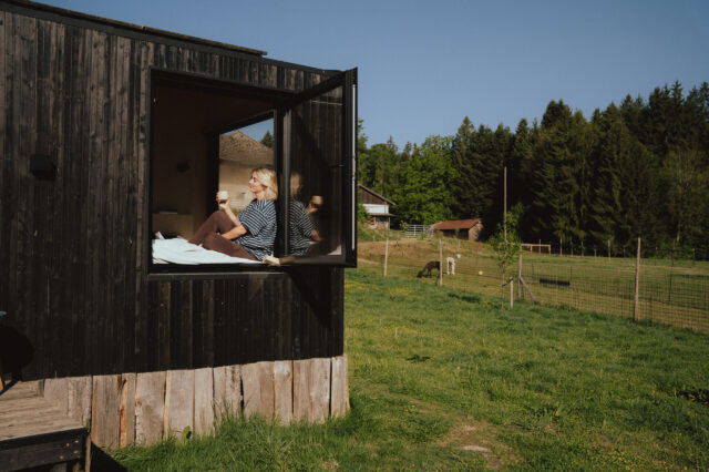 Frau trinkt Kaffee im Fenster einer Cabin und schaut in die Sonne