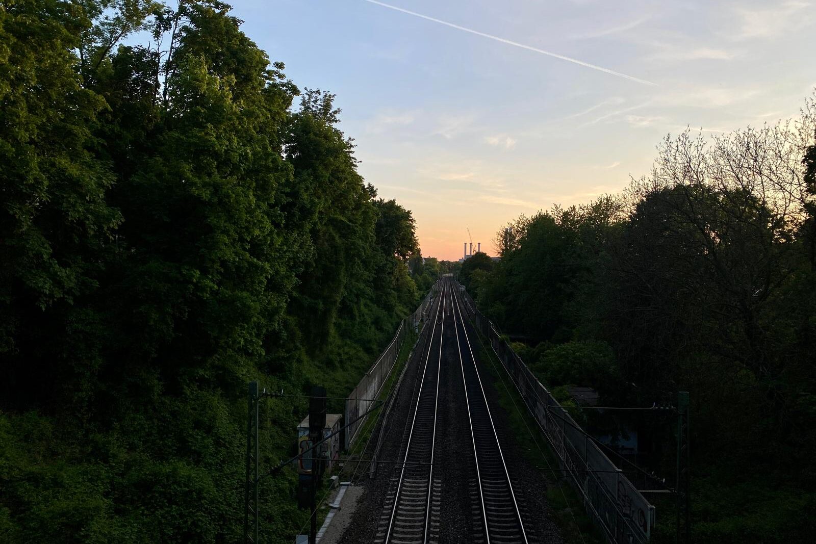 Blick über ein Gleisbett und ins Grüne vom Schmederersteg bei Sonnenuntergang in München.