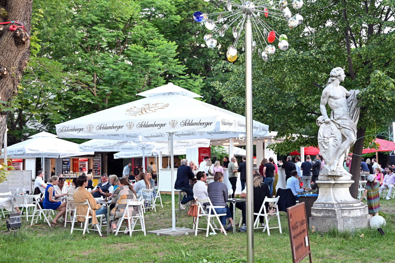 Menschen sitzen auf Sesseln und Liegestühlen unter Sonnenschirmen im Park des Palais Auerspergs in Wien beim Palais Freiluft Pop-up