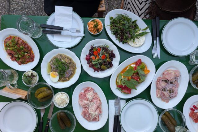 ein gefüllter Tisch mit verschiedenen Heurigen-Speisen im Gastgarten der Buschenschank in Residence in Wien Grinzing