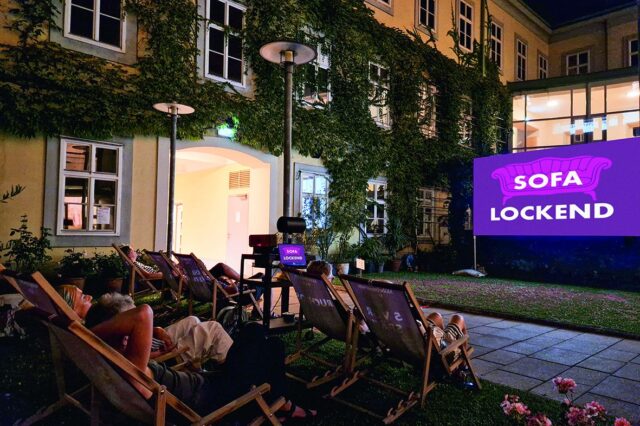 Open Air in Wien: Eine Leinwand im Innenhof des Möbelmuseums, davor Liegestühle mit Zuschauer*innen