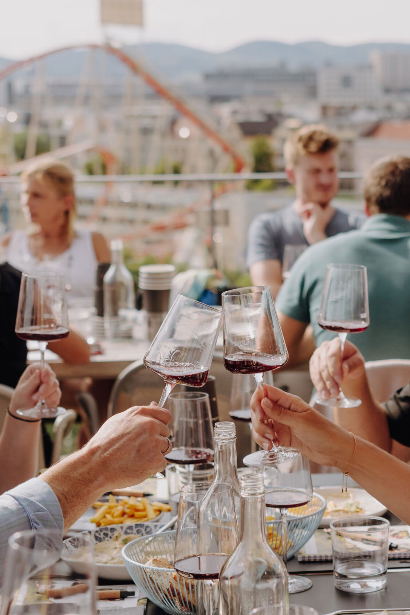 Menschen sitzen im Sommer im Freien, essen und stoßen mit einem Glas Rotwein an