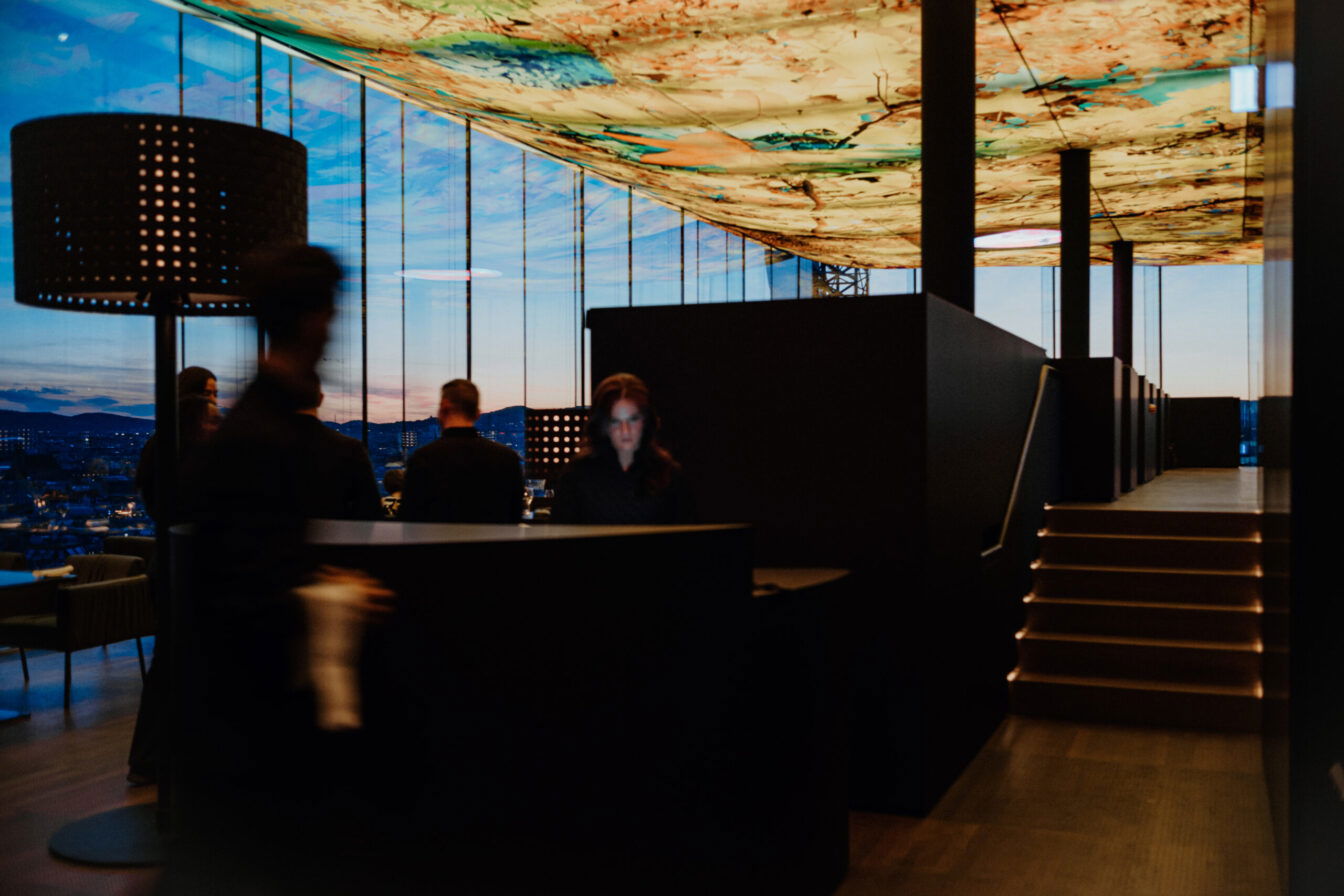 Blick aus dem Restaurant Das Loft in Wien auf das Interieur und durch die Glasfenster auf den Sonnenuntergang in Wien