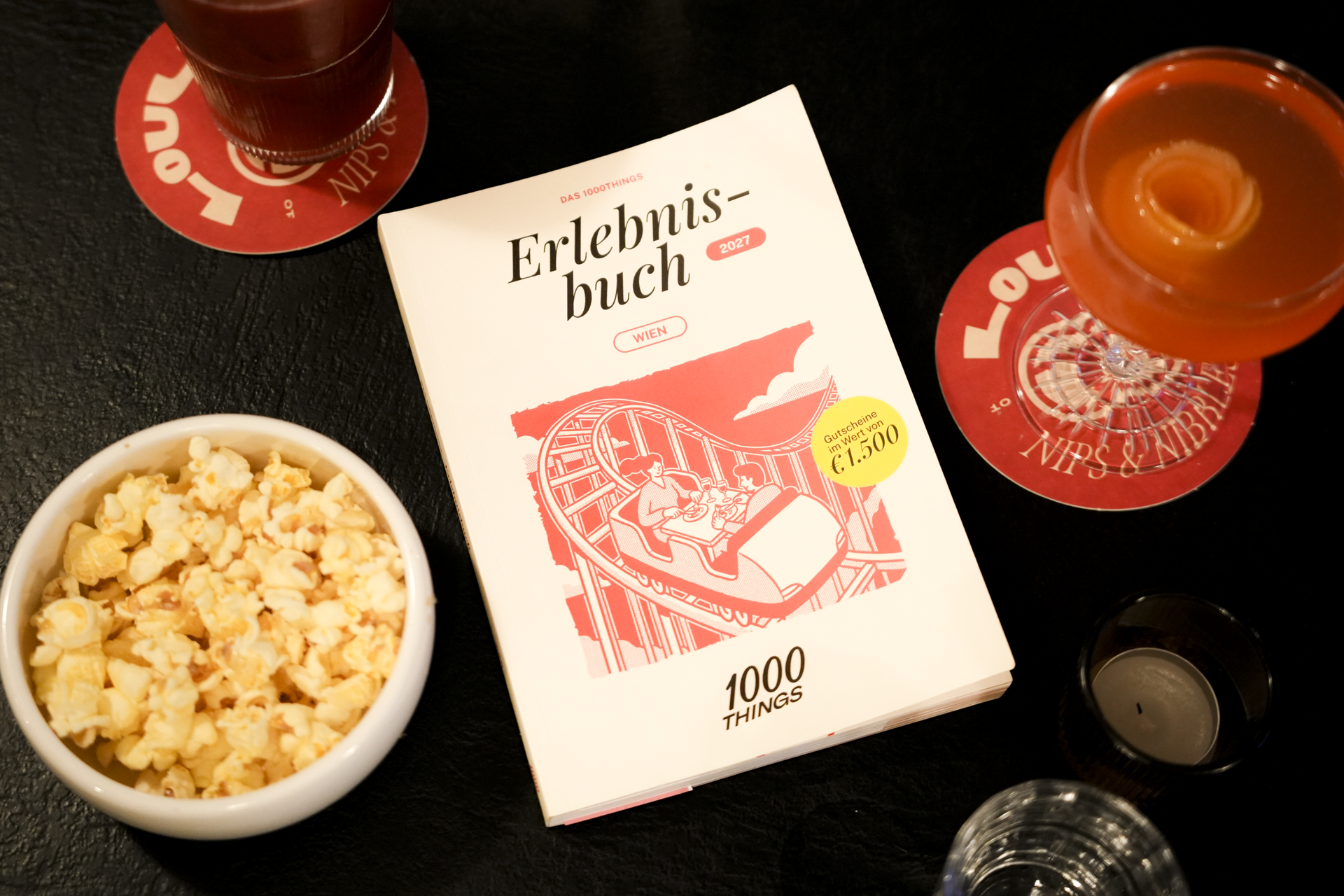 das 1000things Erlebnisbuch Wien 2027 neben Popcorn und Cocktails
