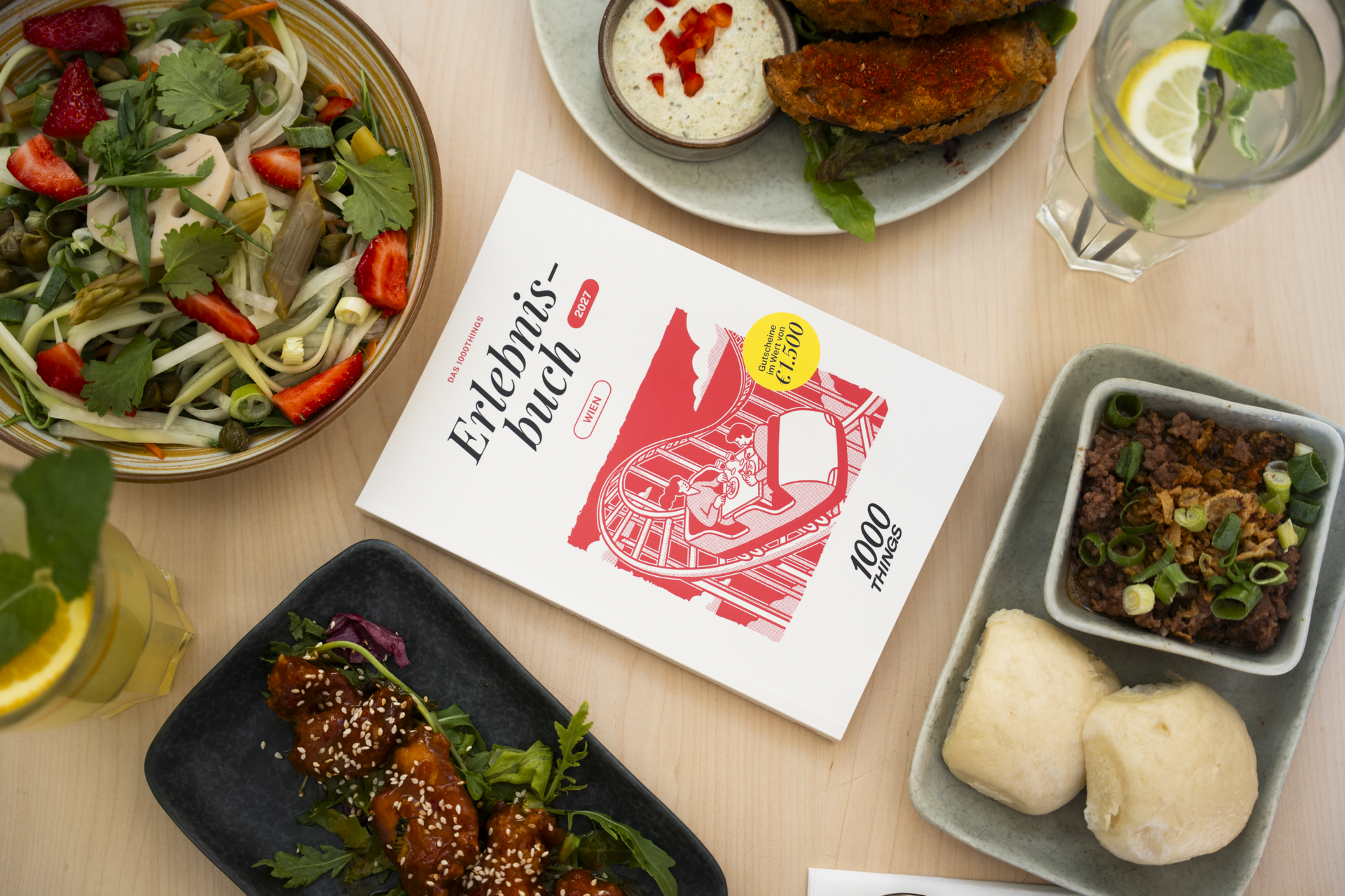 1000things Erlebnisbuch auf einem Tisch neben Essen
