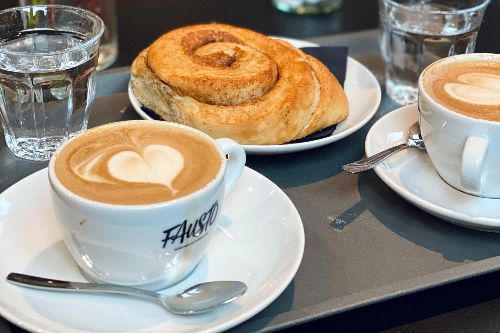 Ein dunkler Tisch gedeckt mit rosa Blumen, Kaffee und Zimtschnecke.