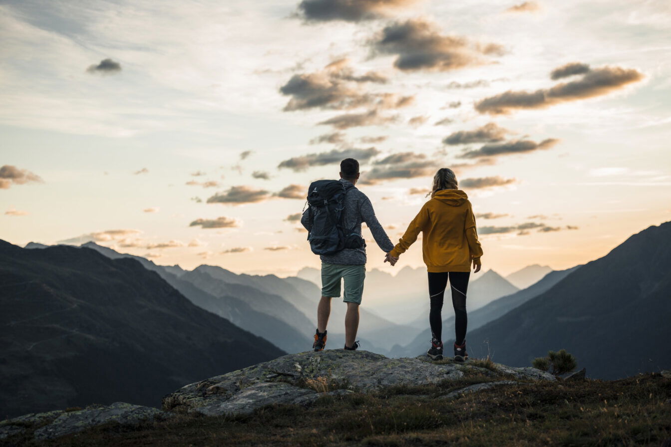 Zwei Personen geben sich die Hand am Berggipfel