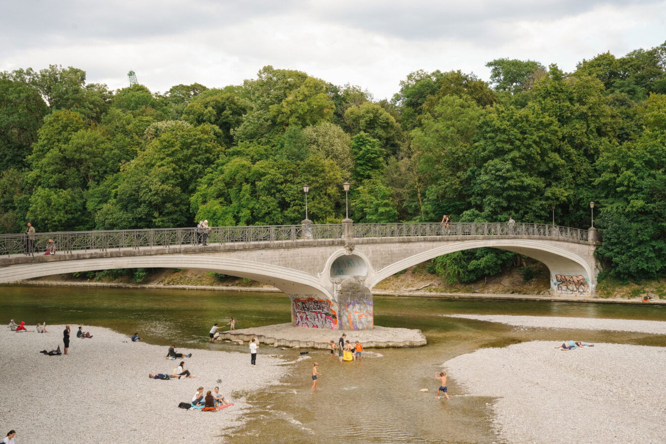 Das Isarufer an der Mariannenbrücke in der Altstadt, Lehel Münchens lädt auf breiten Kiesstränden zum Sonnen, Entspannen und Füße ins Wasser halten ein.
