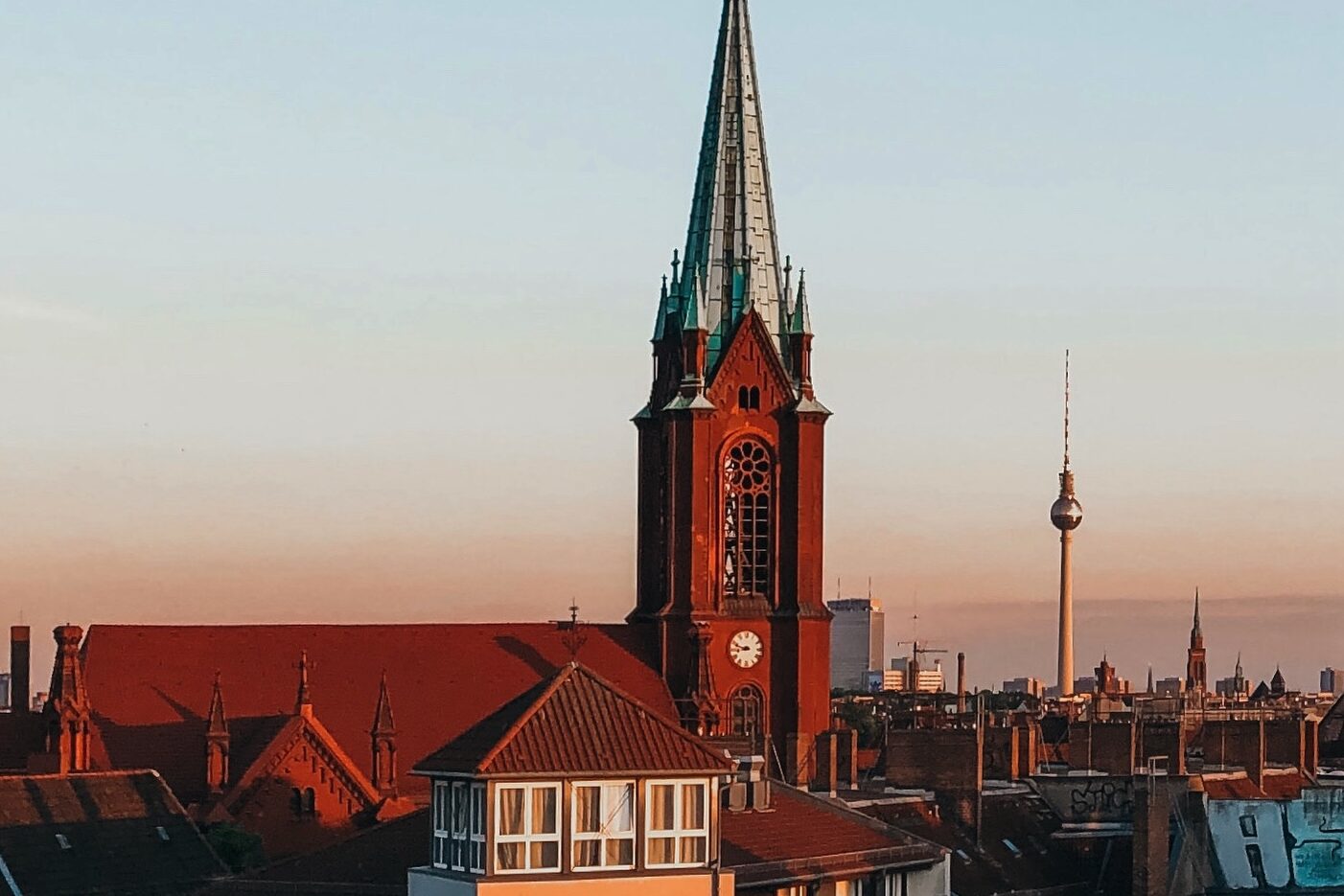 Blick auf die Gethsemanekirche im Berliner Stadtteil Prenzlauer Berg bei Sonnenuntergang mit dem Berliner Fernsehturm im Hintergrund – architektonisches Highlight im Prenzlauer Berg Guide und beliebter Fotospot in Berlin.