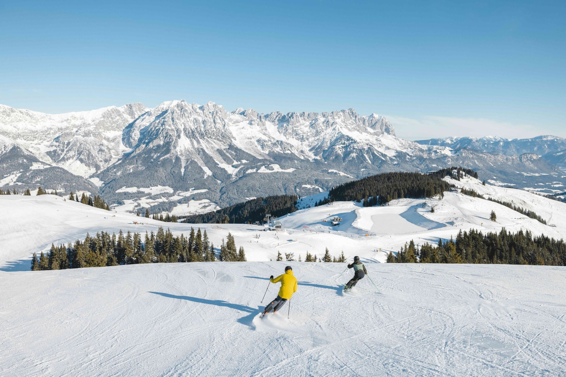 Zwei Skifahrer auf der breiten Piste mit Blick Wilder Kaiser