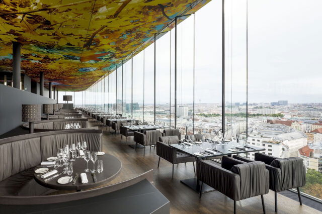 Blick aus dem Restaurant Das Loft über Einrichtung und Möbel und durch große Glasfenster hinaus auf die Skyline von Wien