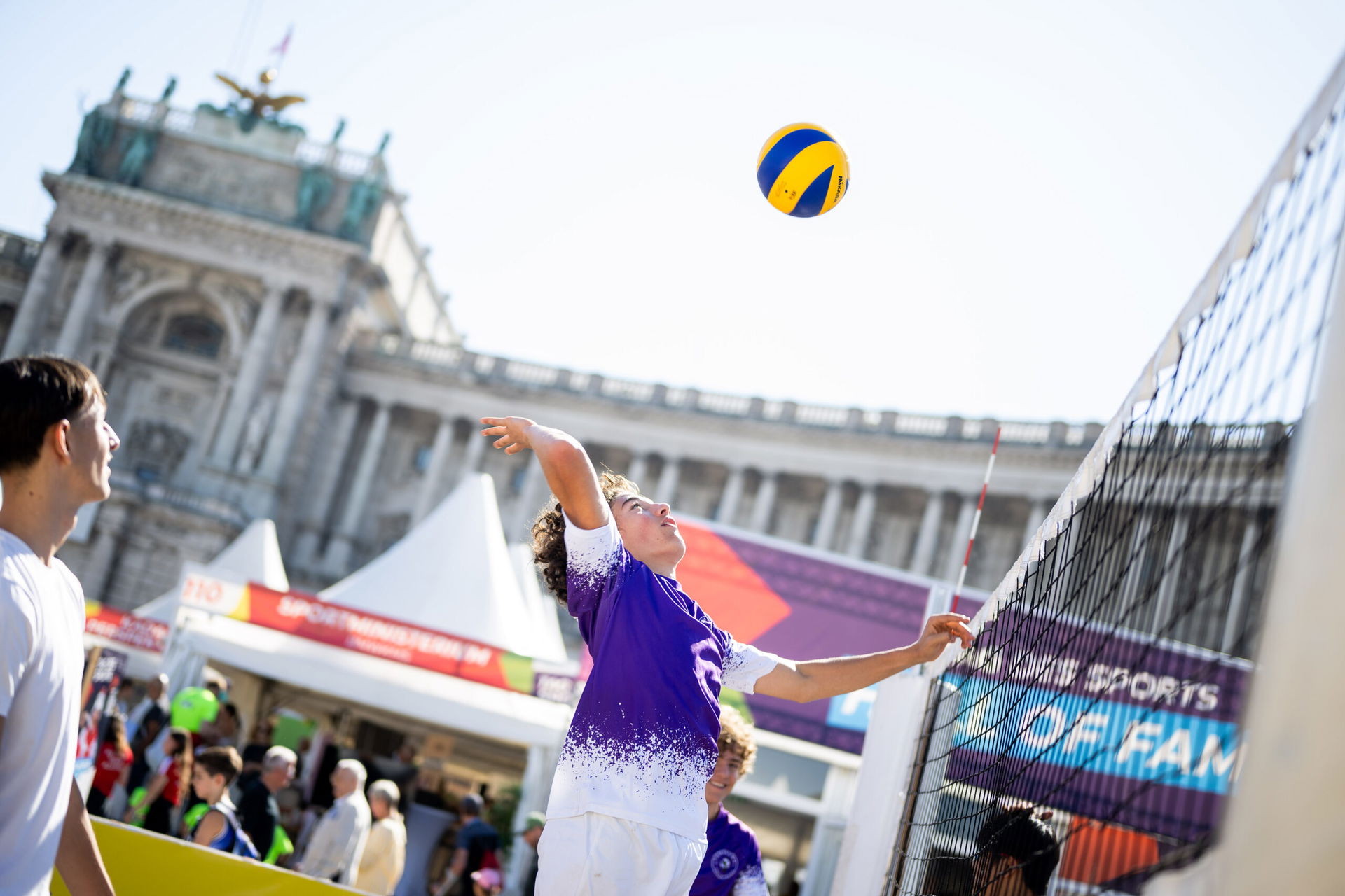 Ein Junge spielt Volleyball mit Hofburg als Kulisse.